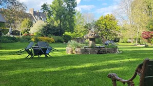 Um jardim bem cuidado com uma fonte de pedra, um banco e uma cadeira de grama.