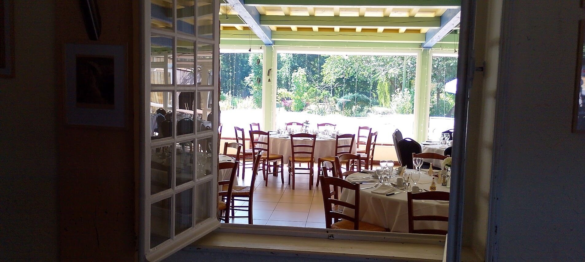 An open doorway leading to a dining area with tables and chairs, a tiled floor, and a view of greenery outside.