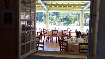 An open doorway leading to a dining area with tables and chairs, a tiled floor, and a view of greenery outside.