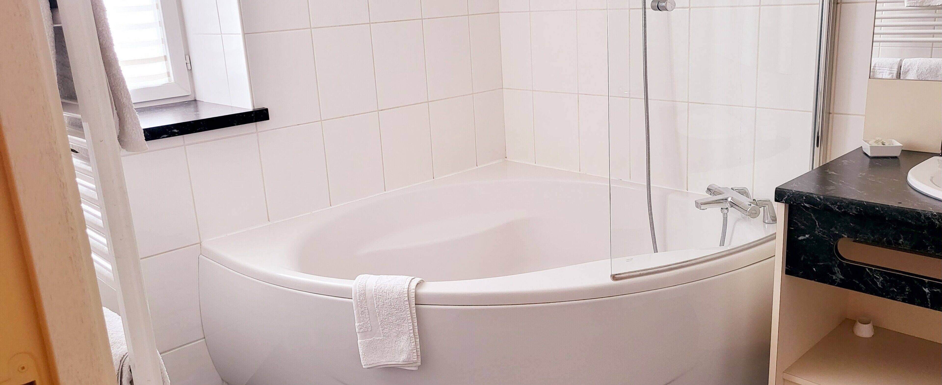A bathroom with a white bathtub, a shower, and a marble countertop.