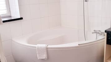 A bathroom with a white bathtub, a shower, and a marble countertop.
