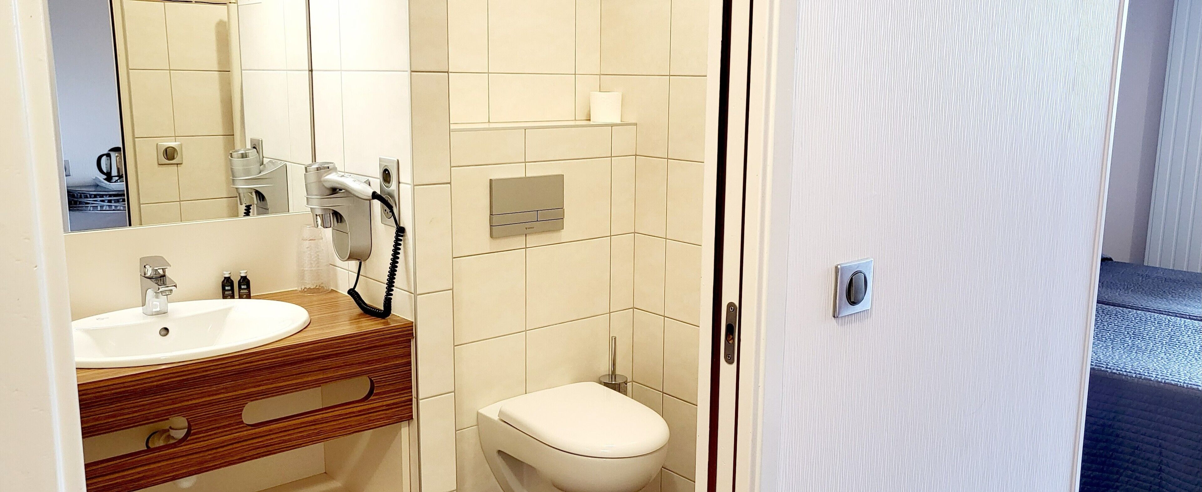A bathroom with a sink, mirror, toilet, and a hairdryer on the wall.