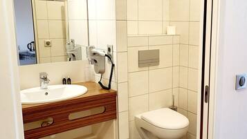 A bathroom with a sink, mirror, toilet, and a hairdryer on the wall.