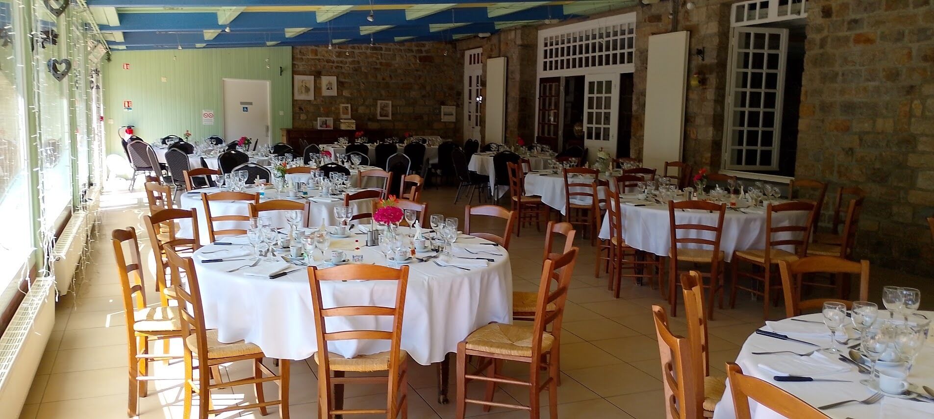 A banquet hall with multiple round tables set for dining, each with white tablecloths and wooden chairs.