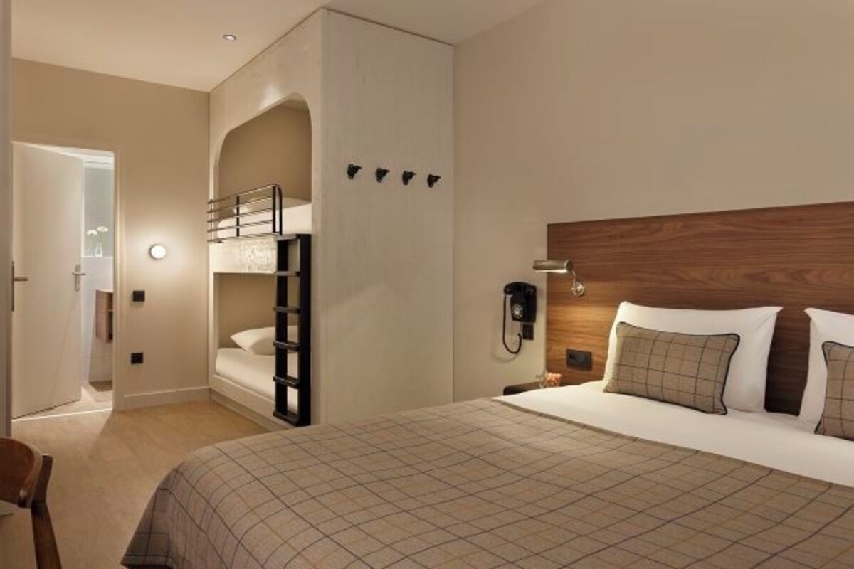 Ett hotellrum med en våningssäng, en sänggavel i trä, en telefon vid sängen och ett rutigt sängöverkast.