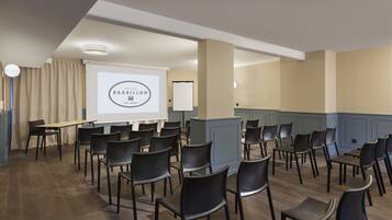 Ett konferensrum med rader av svarta stolar, en projektorduk som visar texten ”MAISON BARBILLON HOTEL” och en whiteboard.
