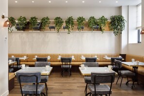 Un restaurante con cabinas, mesas y sillas. Hay plantas en la pared y una ventana a la derecha.