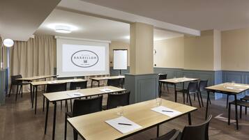 A conference room with multiple tables and chairs, a projector screen displaying a presentation, and a large pillar.