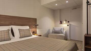 A bedroom with a large bed, a smaller bed, a nightstand, a bedside table, and a wall-mounted shelf with a lamp.