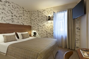 Una habitación de hotel con una cama grande, cabecera de madera, televisor de pantalla plana montado en la pared y una ventana con cortinas.