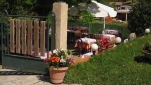 A gated outdoor area with a table and chairs, surrounded by greenery and a stone pillar with a spherical top. - Hotel Bayle (Belcaire)