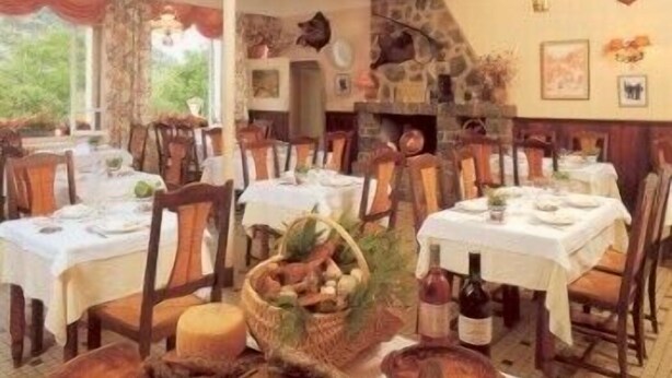 A restaurant with multiple tables and chairs, stone walls, and a rustic interior. - Hotel Bayle (Belcaire)