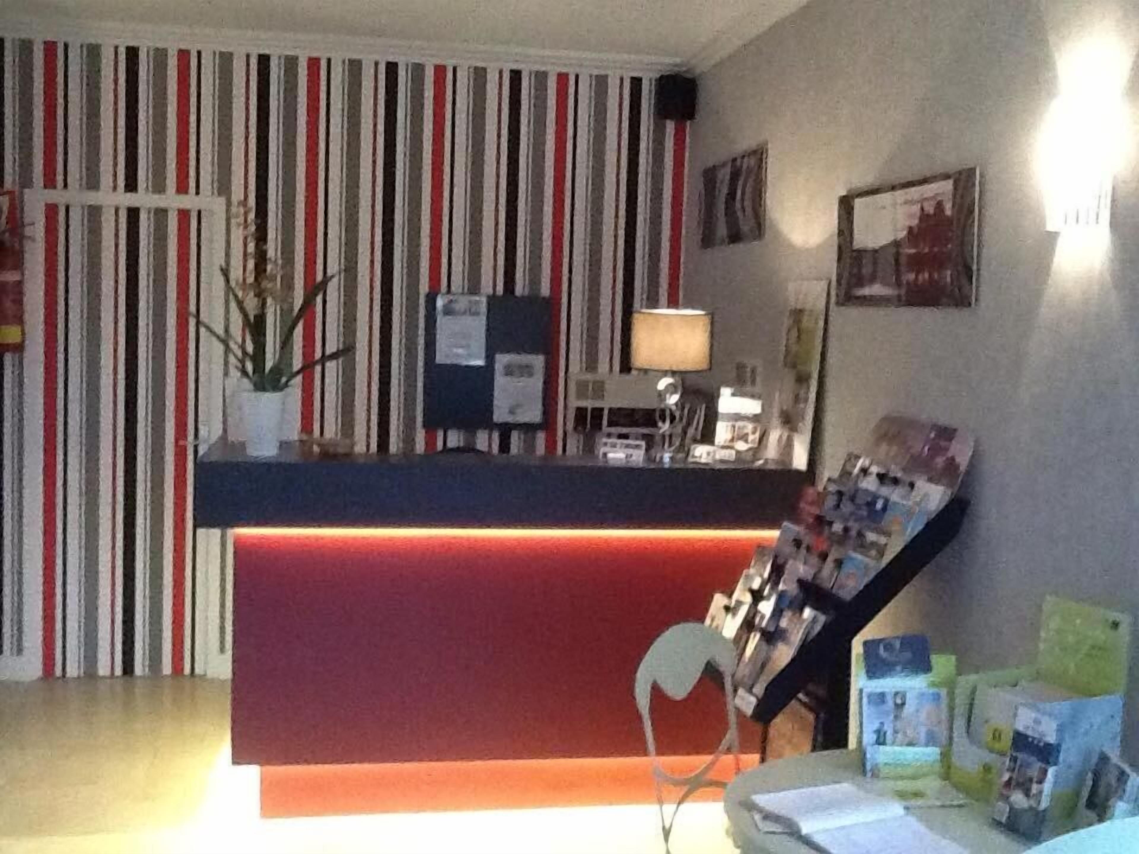 Een receptiebalie met een rode toonbank, een witte vaas met bloemen, een lamp en een stoel.