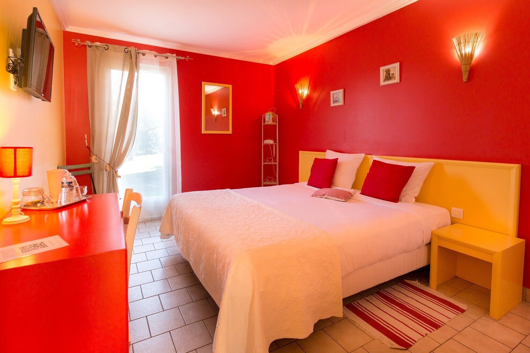A hotel room with a bed, bedside table, and a desk with a lamp.