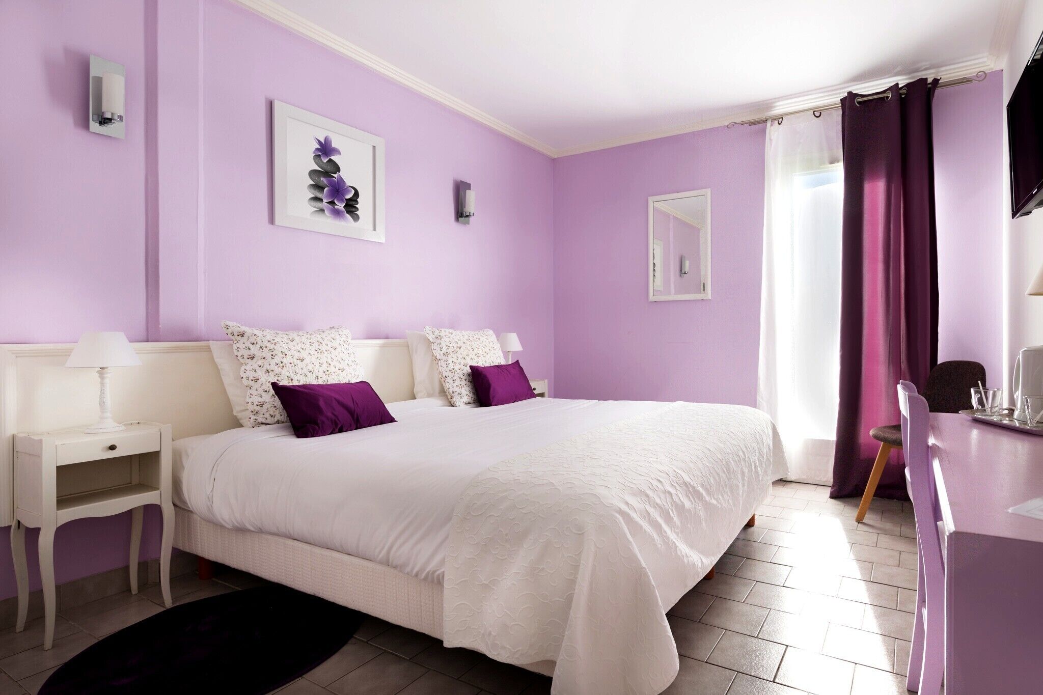 Un dormitorio con una cama grande, un escritorio y una silla. Hay dos lámparas de pared y una ventana con cortinas.