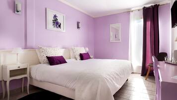 Une chambre avec un grand lit, un bureau et une chaise. Il y a deux appliques murales et une fenêtre avec des rideaux.