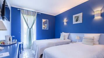 A room with two beds, a desk with a chair, a TV, and a window with curtains.