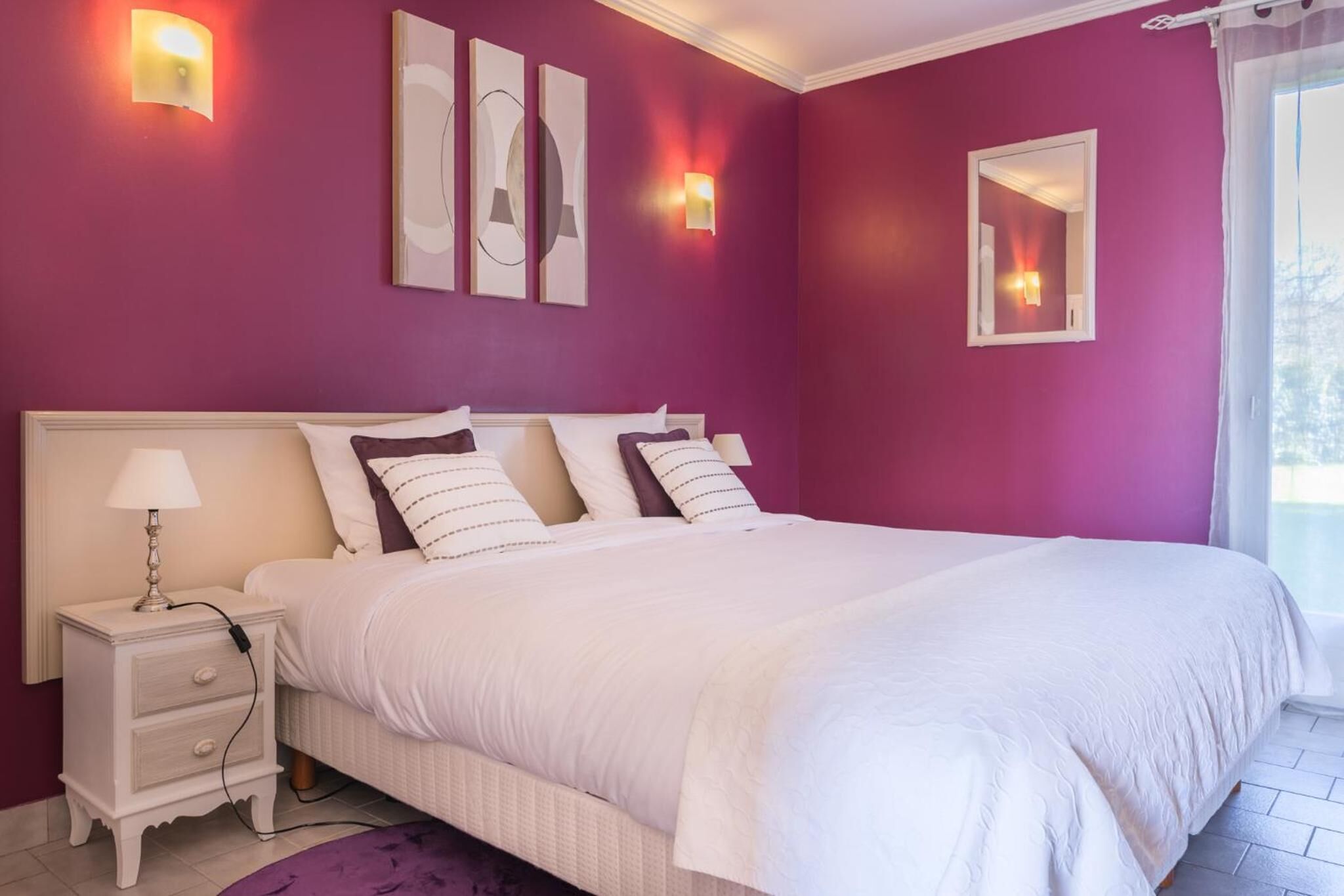 A bedroom with a large bed, white bedding, a nightstand with a lamp, and wall-mounted lights.
