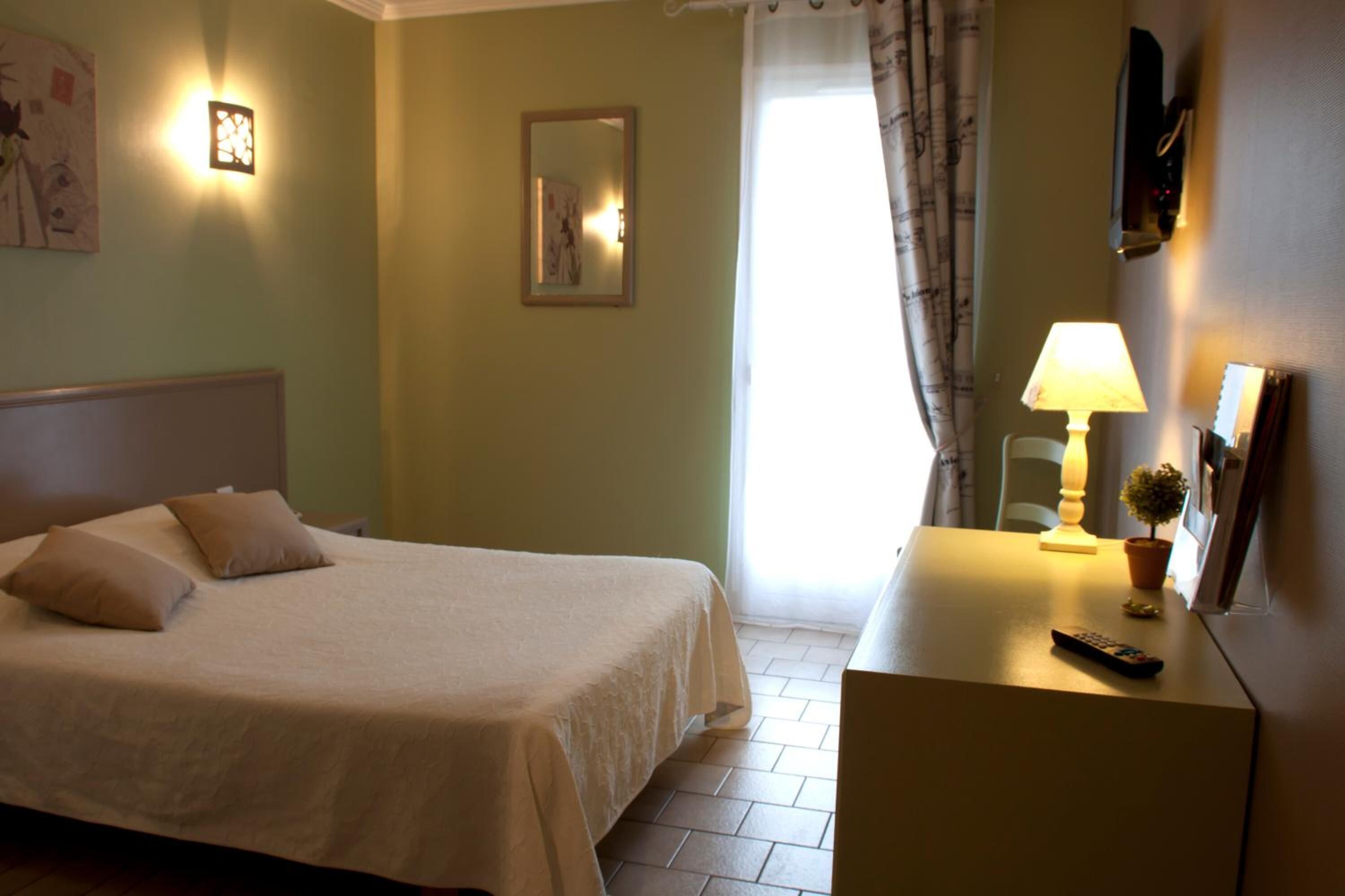 Une chambre d’hôtel avec un lit, une lampe de chevet et une petite table sur laquelle se trouve une télécommande.