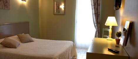 Habitación de hotel con cama, lámpara de noche y una mesita con control remoto.