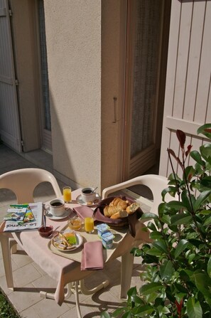 Un área de comedor al aire libre con una mesa preparada para el desayuno, incluyendo croissants, jugo y un periódico.