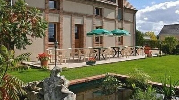 Una casa de dos pisos con techo de tejas, piscina y mobiliario exterior con sombrillas.