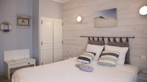 Un dormitorio con cabecera de madera, cama con almohadas a rayas, mesita de noche y estante con un salvavidas y un cuadro enmarcado.