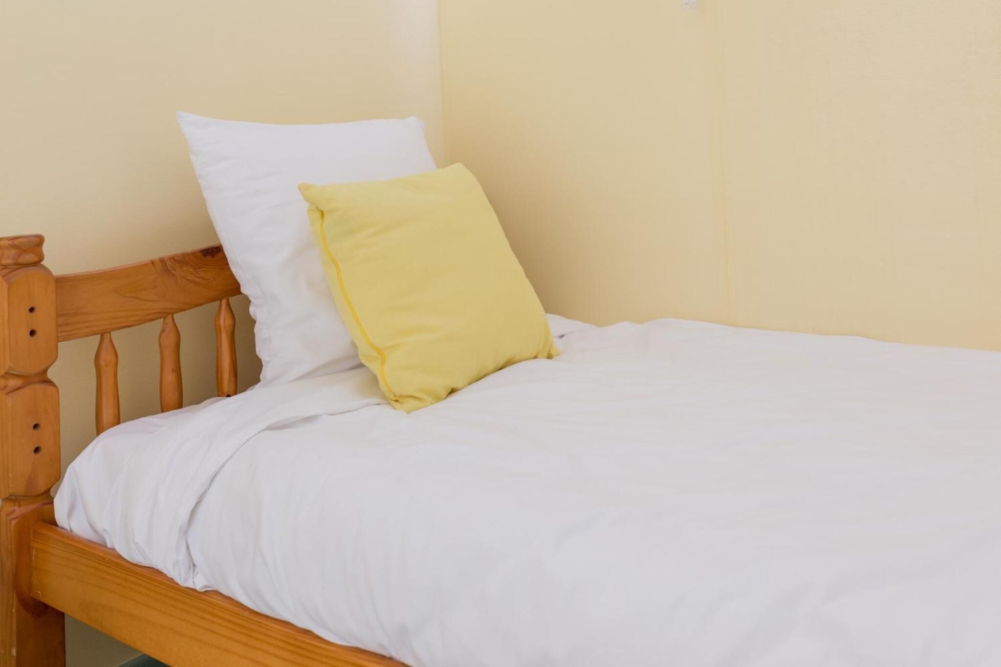A single bed with a wooden headboard, white bedding, and a yellow pillow.