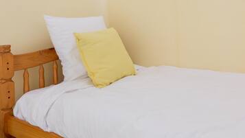 A single bed with a wooden headboard, white bedding, and a yellow pillow.