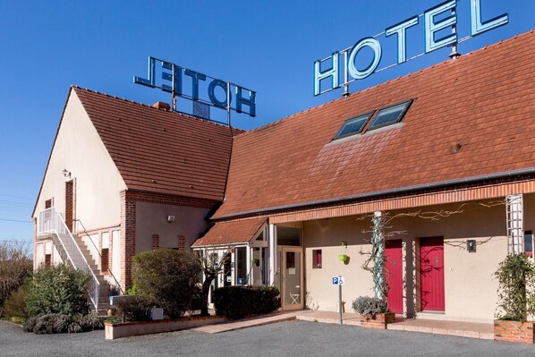 Un hotel con un cartel grande que dice 'HOTEL', una escalera que conduce a la entrada y un cartel de 'P' que indica una zona de estacionamiento.