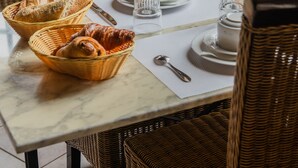 Ein Esstisch ist gedeckt mit Brot, Tellern und einem Teekessel, umgeben von Korbstühlen.