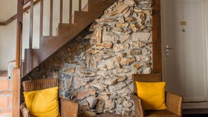 Eine Treppe mit hölzernen Geländern, einer Steinwand und Korbstühlen mit gelben Kissen.