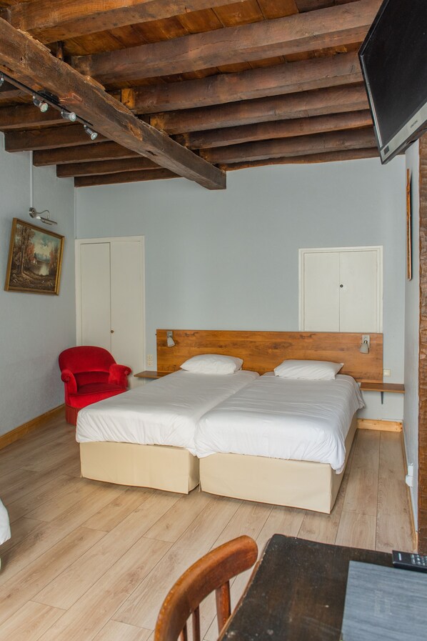A bedroom with two beds, wooden ceiling beams, a red chair, and a wooden table.