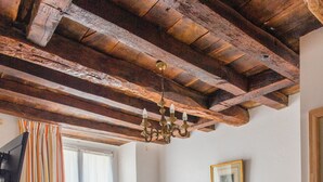 Ein Schlafzimmer mit zwei Betten, Holzbalken an der Decke, einem Chandelier, einem gerahmten Bild an der Wand und einem Fenster mit Vorhängen.