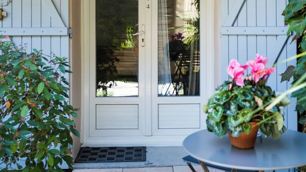 Une entrée d’immeuble avec une porte, une petite table avec des chaises et une plante en pot.