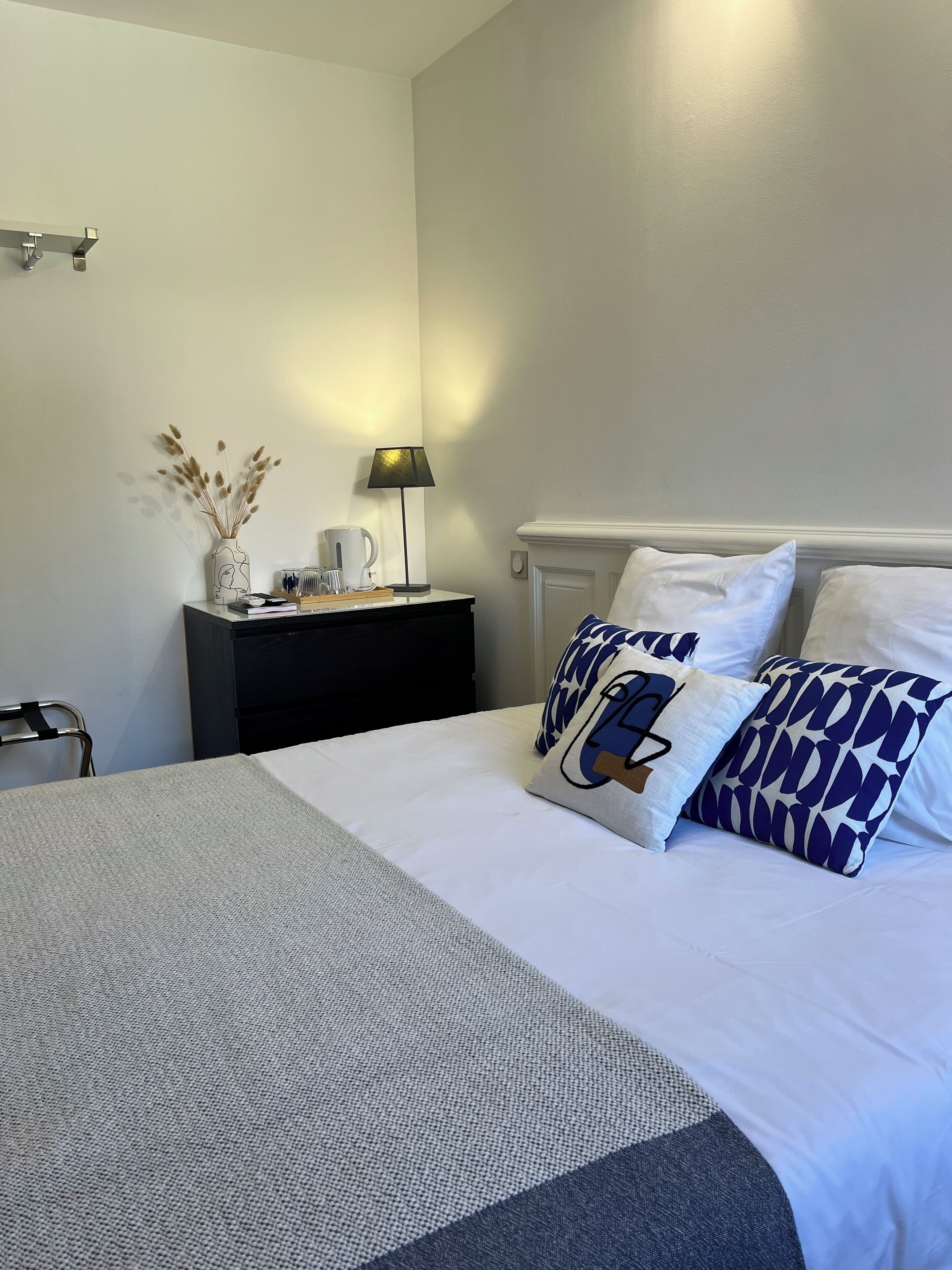 Ein ordentlich eingerichtetes Hotelzimmer mit einem Bett, einem Nachttisch mit Lampe und einem Sessel.