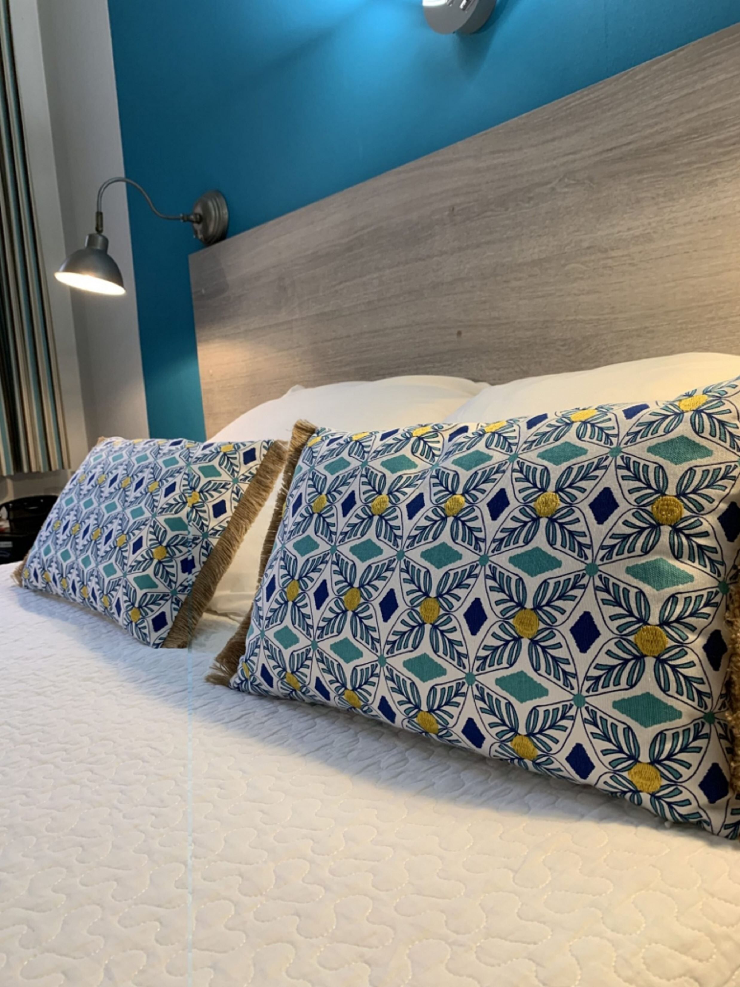 Un lit avec des coussins à motifs et une tête de lit adossée à un mur bleu.