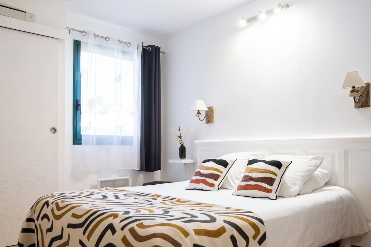 A bedroom with a bed, a bedside table, a lamp, and a window with curtains.
