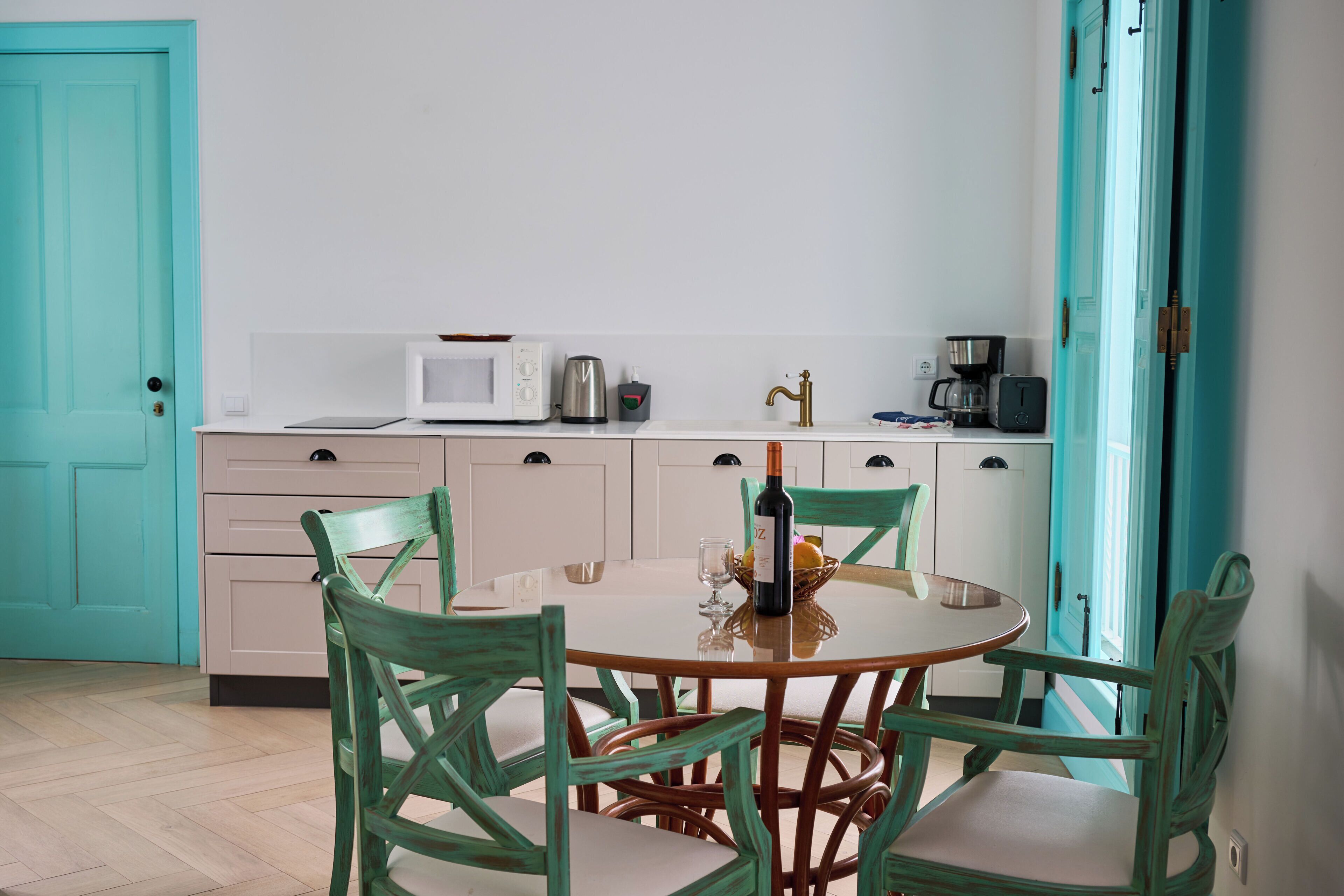 Une cuisine avec une table ronde, quatre chaises, un four à micro-ondes, une machine à café et une bouteille de vin.