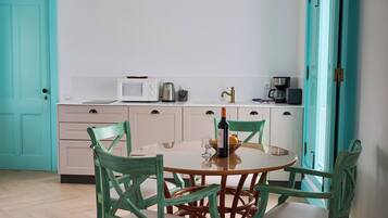 Une cuisine avec une table ronde, quatre chaises, un four à micro-ondes, une machine à café et une bouteille de vin.