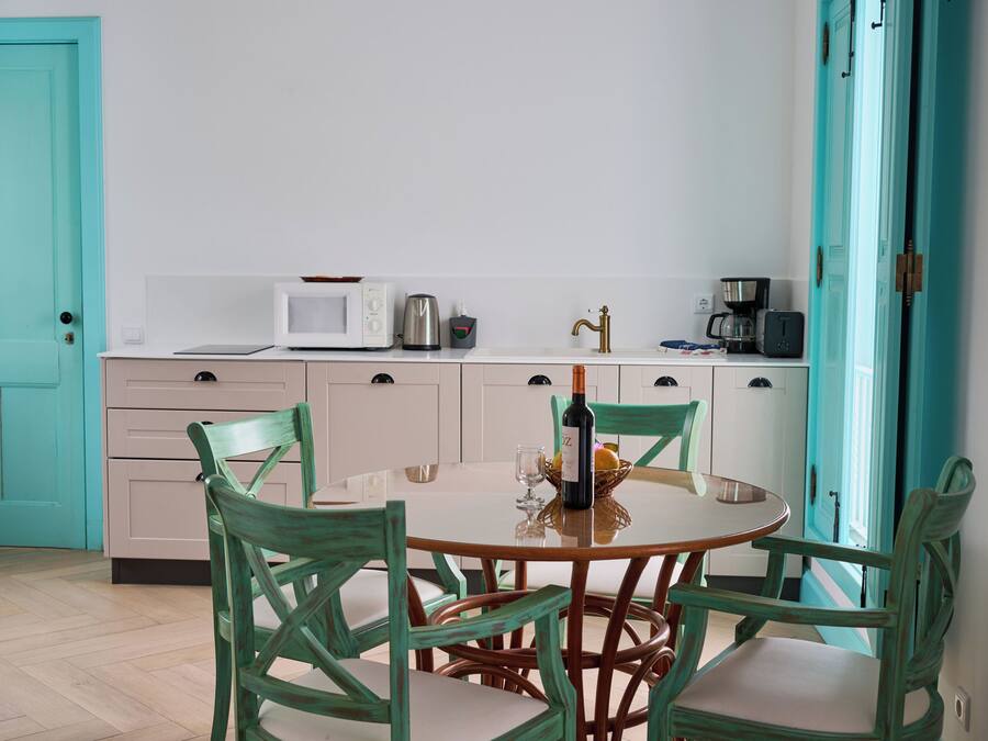 Une cuisine avec une table ronde, quatre chaises, un four à micro-ondes, une machine à café et une bouteille de vin.