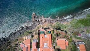 Vista aerea di una proprietà costiera con diversi edifici, un litorale roccioso e acque blu cristalline.