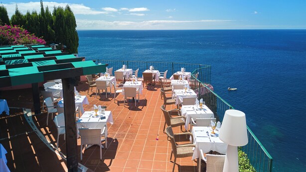 Una terrazza con tavoli e sedie che si affaccia sul mare, con vista sull'oceano e una barca in lontananza.
