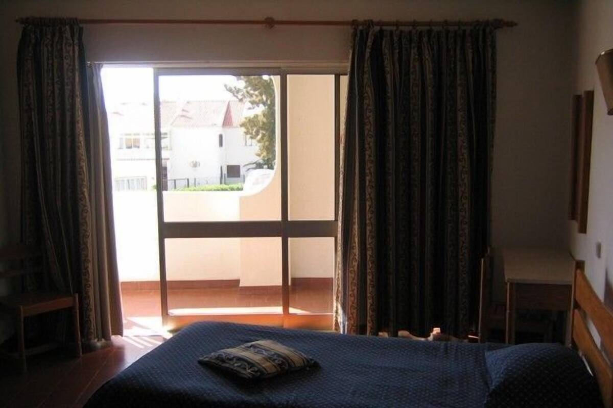 Ein Schlafzimmer mit Bett, einem Fenster mit Vorhängen und Blick ins Freie.