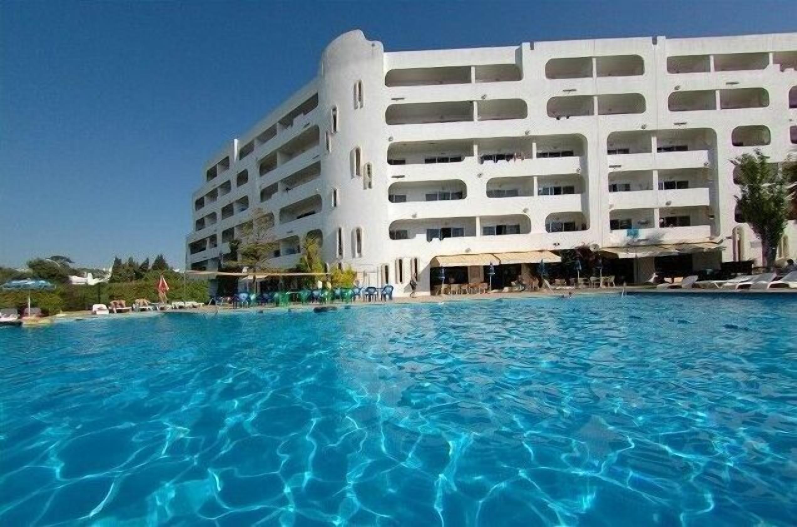 A large hotel with multiple balconies and a swimming pool in the foreground.