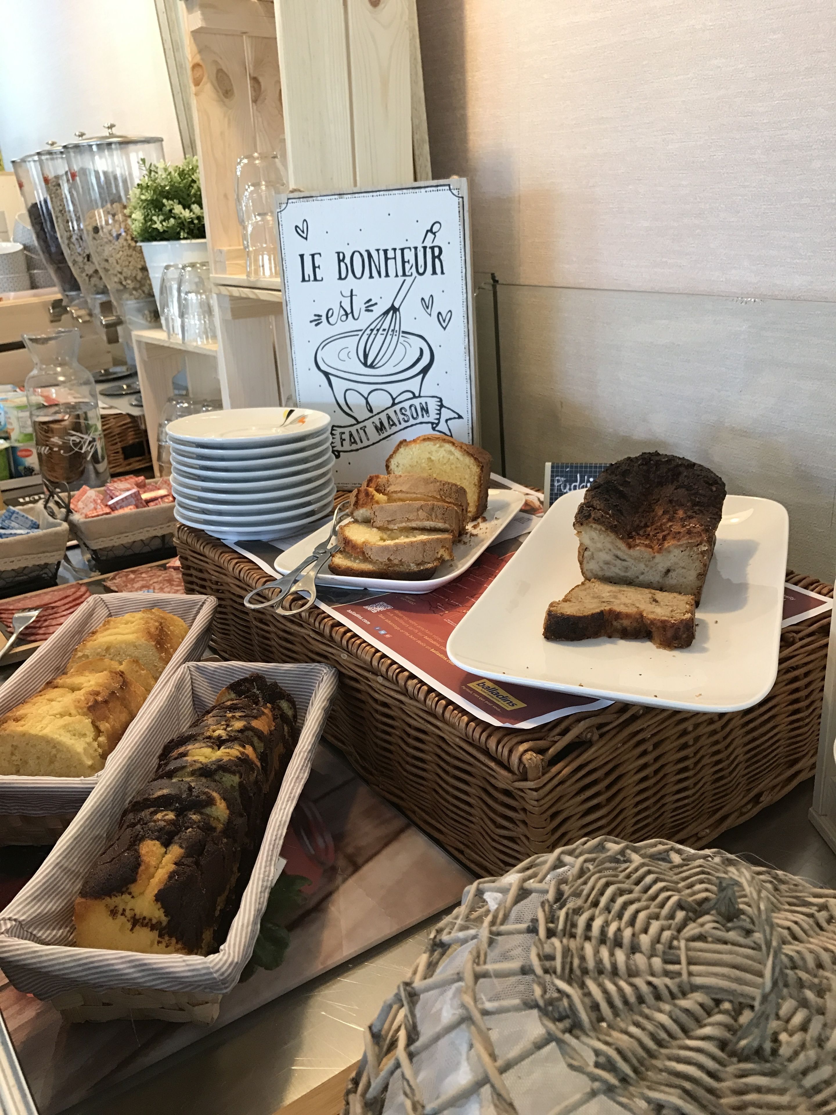 Een bakkerijdisplay met diverse broden en gebak, een bordje met de tekst 