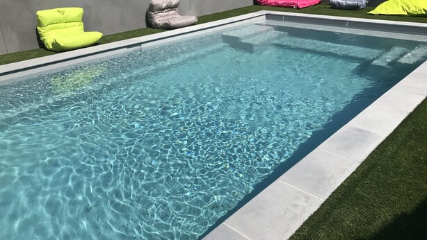 A rectangular swimming pool with clear water, surrounded by a tiled deck and artificial grass. - Kyriad Direct Agen-Castelculier (Castelculier)
