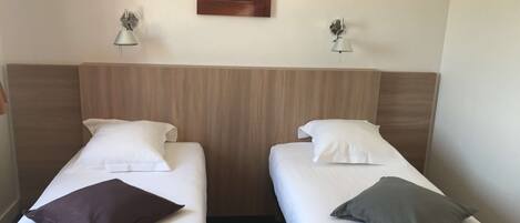 Habitación de hotel con dos camas individuales, cada una con una almohada y una lámpara de noche.
