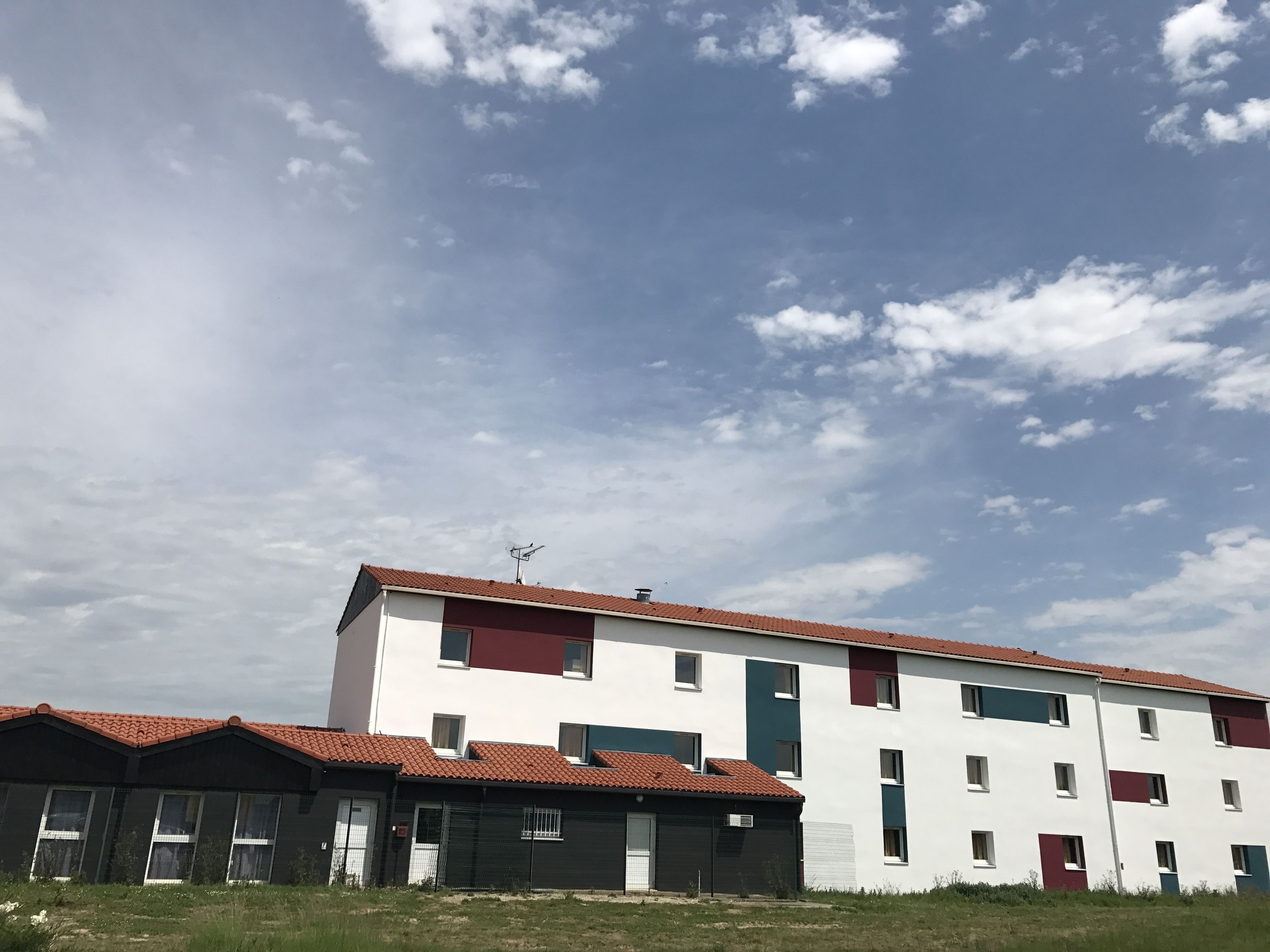 A multi-story building with a red-tiled roof, white walls, and a mix of green and red accents.