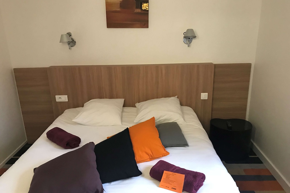 A neatly made bed with a wooden headboard, two wall-mounted lamps, and a small trash bin to the side.